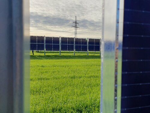 Blick zwischen zwei Agri-PV anlagen auf ein Feld auf dem auch Agri-PV Elemente stehen.