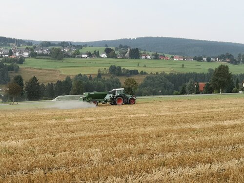 Auf einem Acker in Deutschland. Ein Traktor fährt in Deutschland über ein gemähtes Getreidefeld und verteilt ein weißbraunes Pulver.
