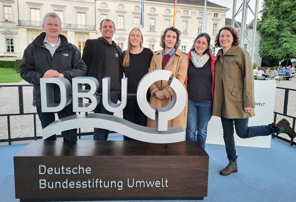 Sechs Personen stehen auf einer Bühne vor Schloss Bellevue hinter dem Logo der Deutschen Bundesstiftung Umwelt