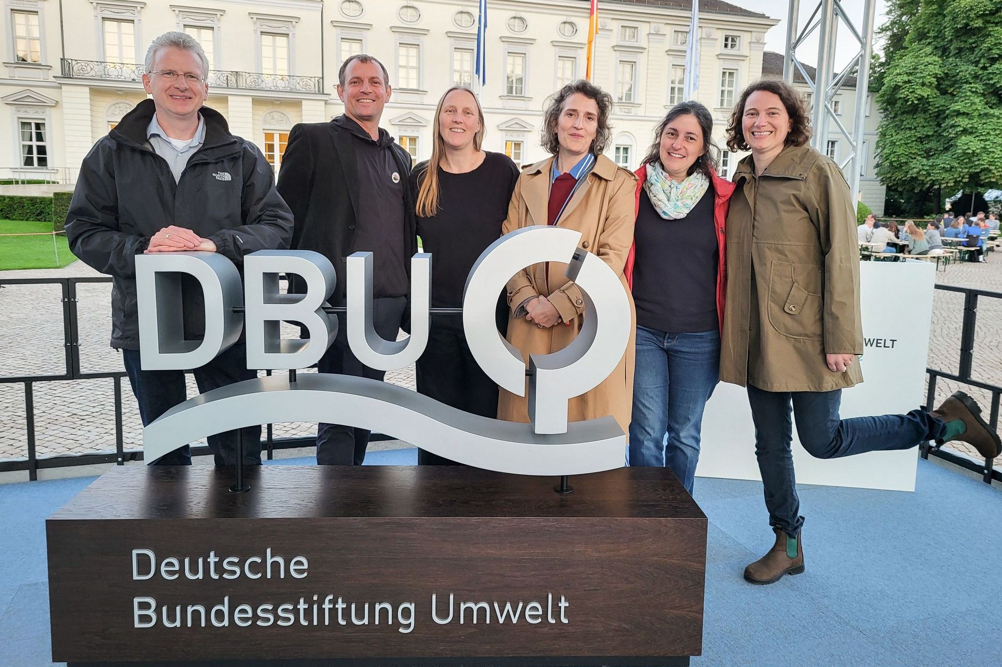 Sechs Personen stehen auf einer Bühne vor Schloss Bellevue hinter dem Logo der Deutschen Bundesstiftung Umwelt