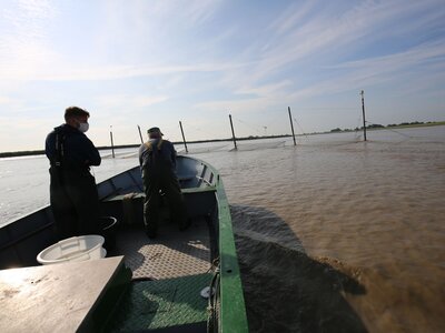 Doktorand Leander Höhne (links) und ein kooperierender Fischer auf dem Weg, das Fanggerät zu kontrollieren. Ein flaches Boot mit zwei Personen auf dem Weg zu einer Reuse
