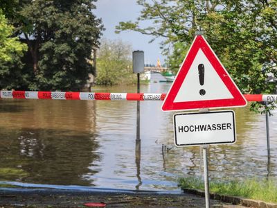 Ein Achtung Hochwasser Schild vor einem überfluteten Weg