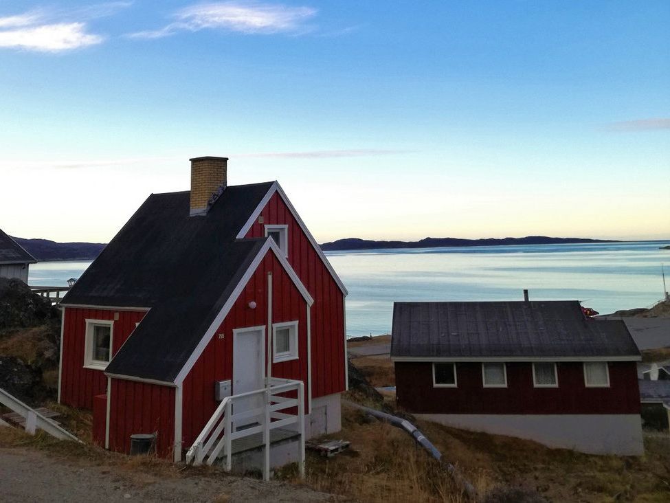 [Translate to English:] Eine Gruppe kleiner Holzhäuser am Wasser auf Grönland.