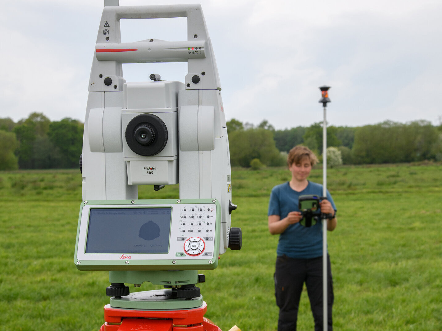 Mit dem Tachymeter messen die Forschenden die Geländehöhen im Moor. Im Vordergrund ein technisches Gerät auf einem Stativ, im Hintergrund eine Person, die ein anderes Gerät hält.