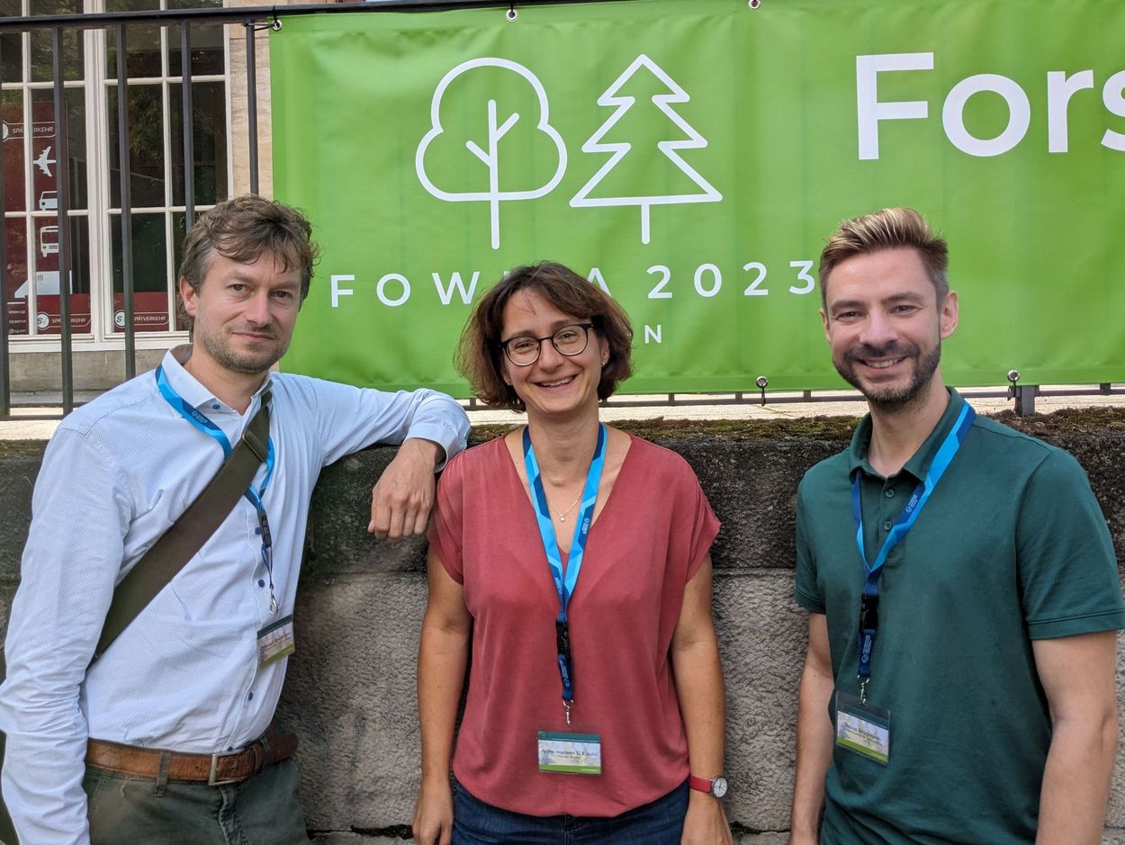 Links steht Herr Christoph Rieckmann, daneben Frau Dr. Anne-Mareen Eisold und rechts Herr Dr. Tobias Brügmann. Im Hintergrund ein grünes Plakat von der FoWiTa
