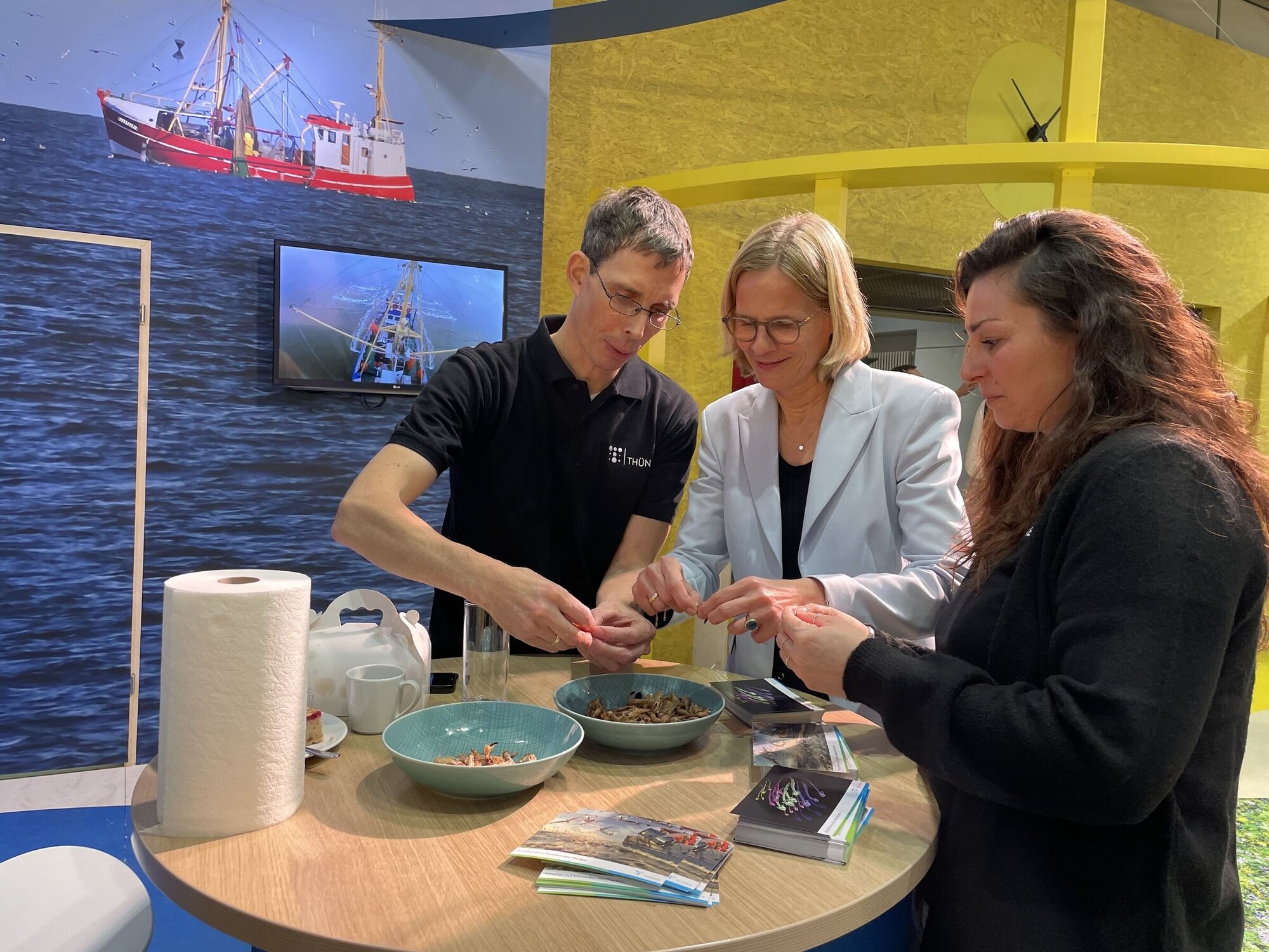 Birgit Kleinschmit, die designierte Präsidentin des Thünen-Instituts, pult Krabben am Stand des Instituts für Seefischerei. Drei Personen versuchen das Krabbenfleisch aus den Nordseekrabbenschalen zu bekommen.