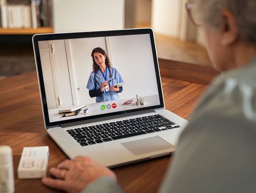 Eine ältere Frau sitzt vor einem Notebook. Auf dem Bildschirm ist eine Ärztin per Videotelefonat zugeschaltet.