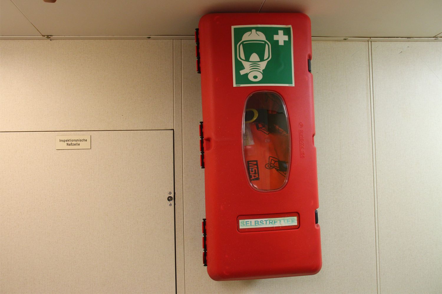 Ein roter Kasten an der Wand in dem ein Selbstretteratemgerät für den Notfall liegt.