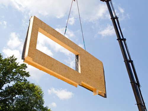 Modulare Bauteile lassen sich wiederverwenden, ohne dass die Holzqualität darunter leidet Ein Teil des Hauses wird mit Hilfe des Krans in die Luft gehoben.