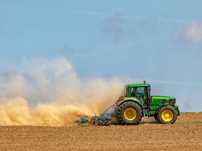 Trockene, wenig bedeckte Böden sind besonders anfällig für Erosion. Traktor, der den Boden mit Scheibenegge bearbeitet und eine riesige gelbe Staubwolke verursacht.