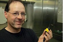 Ein Wissenschaftler zeigt einen schwarzen Satellitentransmitter, den er in der linken Hand hält.