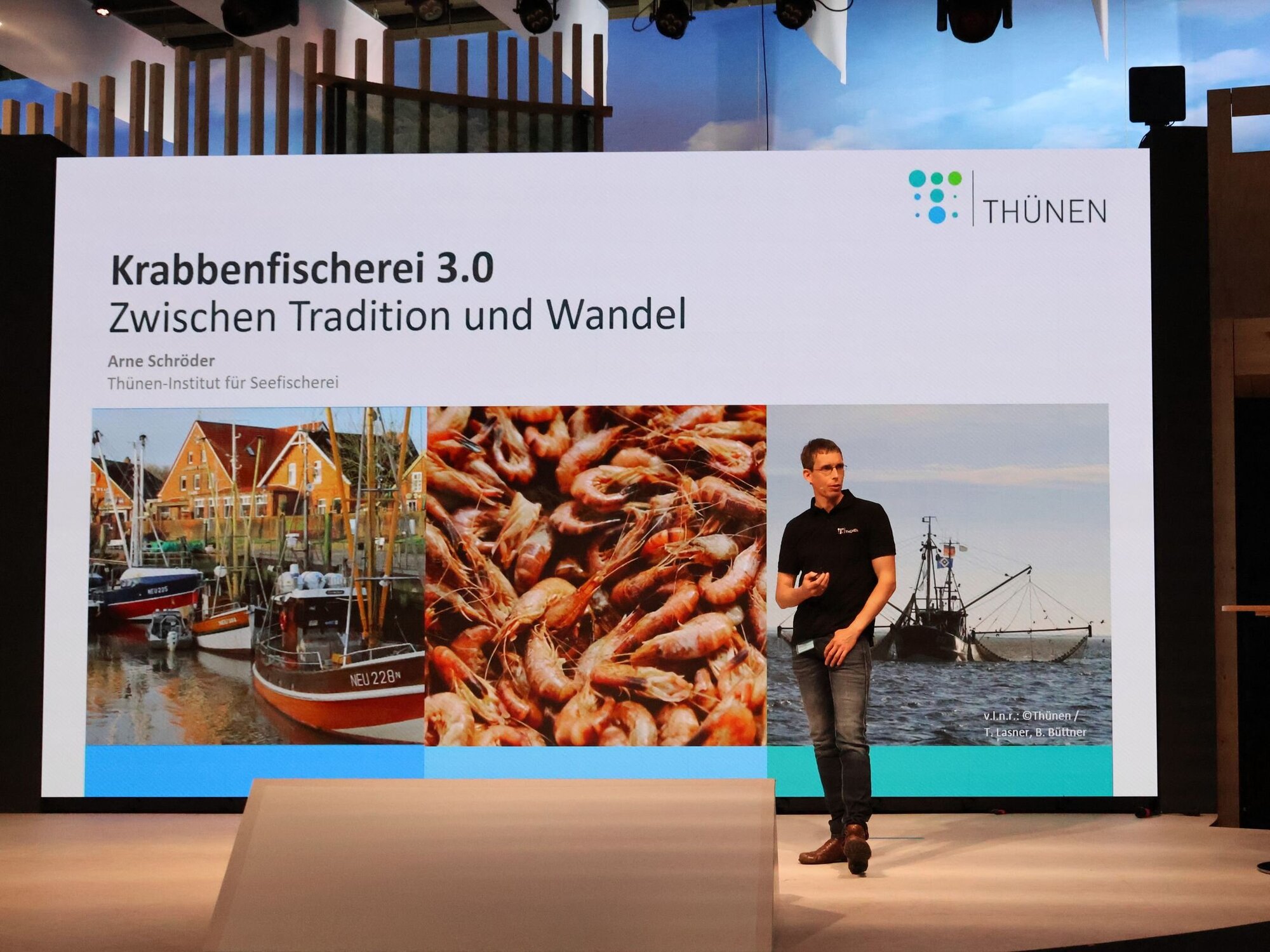 Auf der Bühne der BMEL-Halle erläutert Arne Schröder vom Thünen-Institut für Seefischerei Details zur Forschung rund um die Krabbenfischerei in der Nordsee. Eine Powerpointfolie auf der Krabbenfischerei 3.0 steht, eine Person steht daneben.