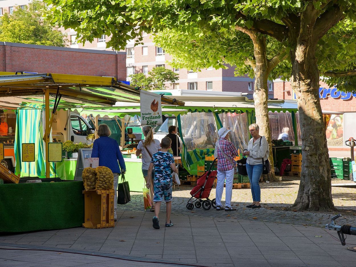 Verschiedene Personen kaufen auf einem Markt ein und unterhalten sich.