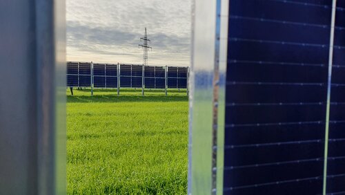 Blick zwischen zwei Agri-PV anlagen auf ein Feld auf dem auch Agri-PV Elemente stehen.