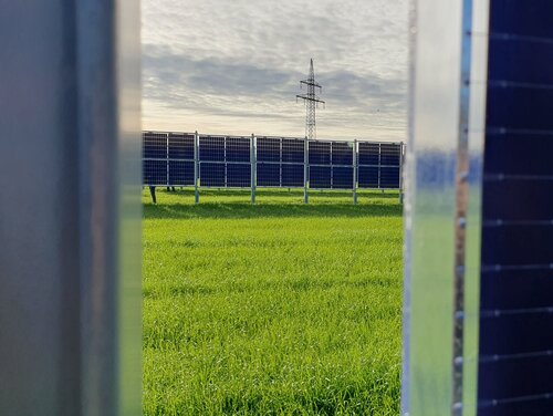 Blick zwischen zwei Agri-PV anlagen auf ein Feld auf dem auch Agri-PV Elemente stehen.