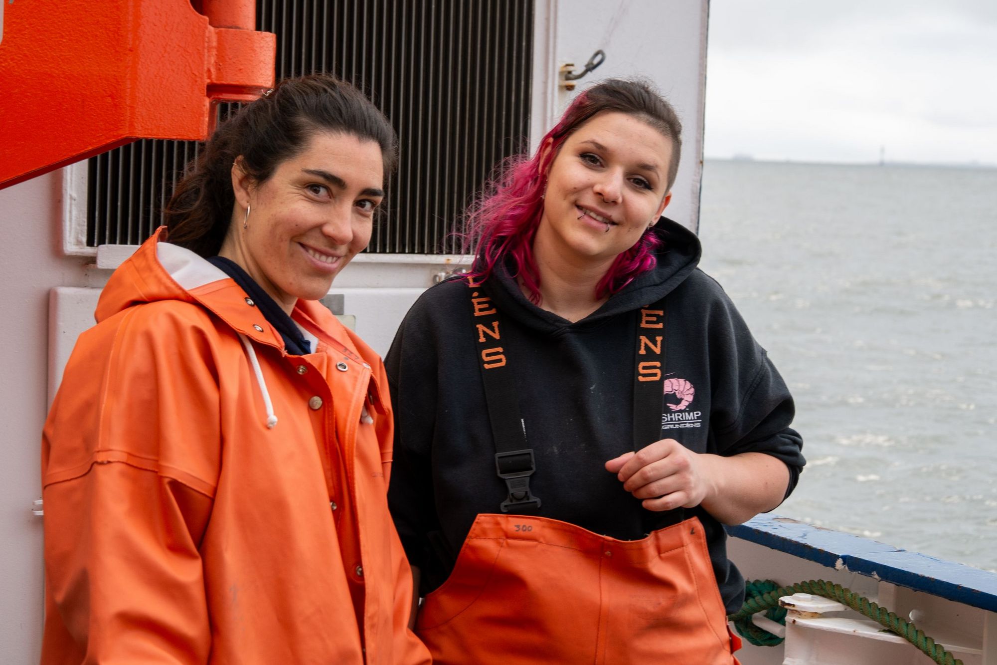 Zwei Frauen in orangenem Ölzeug an Deck.