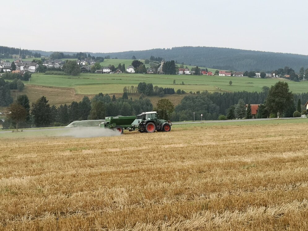 Auf einem Acker in Deutschland. Ein Traktor fährt in Deutschland über ein gemähtes Getreidefeld und verteilt ein weißbraunes Pulver.
