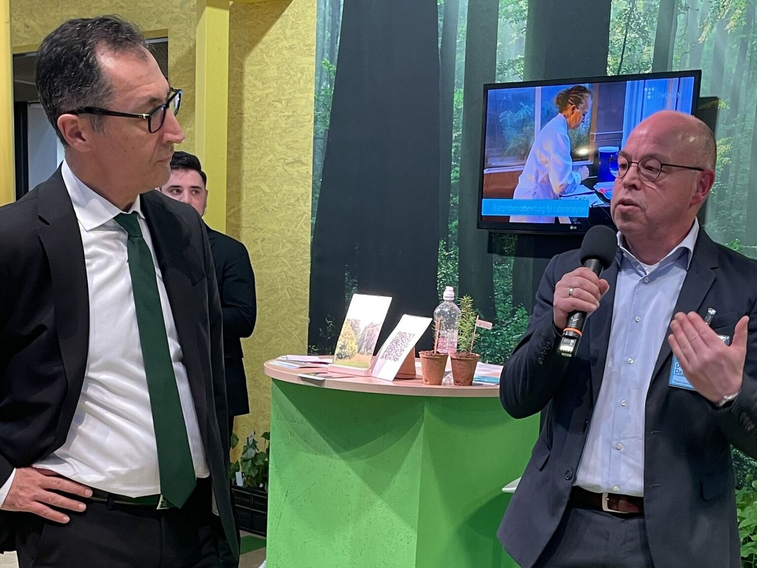 Bernd Degen, Institutsleiter des Thünen-Inistituts für Forstgenetik, erläutert Minister Cem Özdemir, wie wir an klimafesten Wäldern forschen. Zwei Personen an einem Messestand.