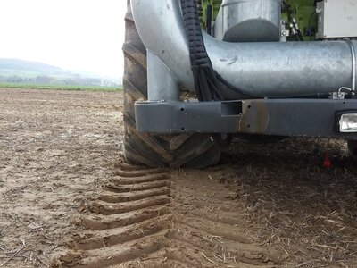 Ein Traktor fährt über den Acker und hinterlässt tiefe Fahrspuren auf dem feuchten Boden.