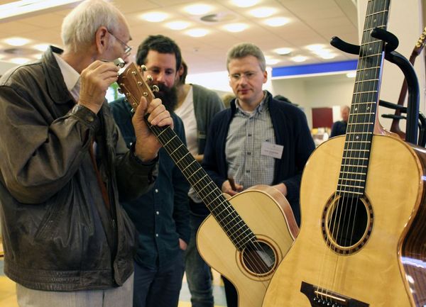 Dieses Bild zeigt drei Männer, die gemeinsam eine Gitarre auf ihre Holzart untersuchen