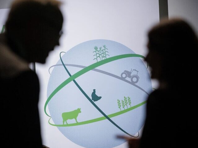 Das GFFA bringt Teilnehmende aus Politik, Wissenschaft, Wirtschaft und Zivilgesellschaft zusammen. Im Vordergrund zwei unscharfe Personen im Schatten, dahinter ist ein Logo zusehen mit einer Kugel, die von Linien umspannt wird auf denen verschiedene Tiere abgebildet sind.