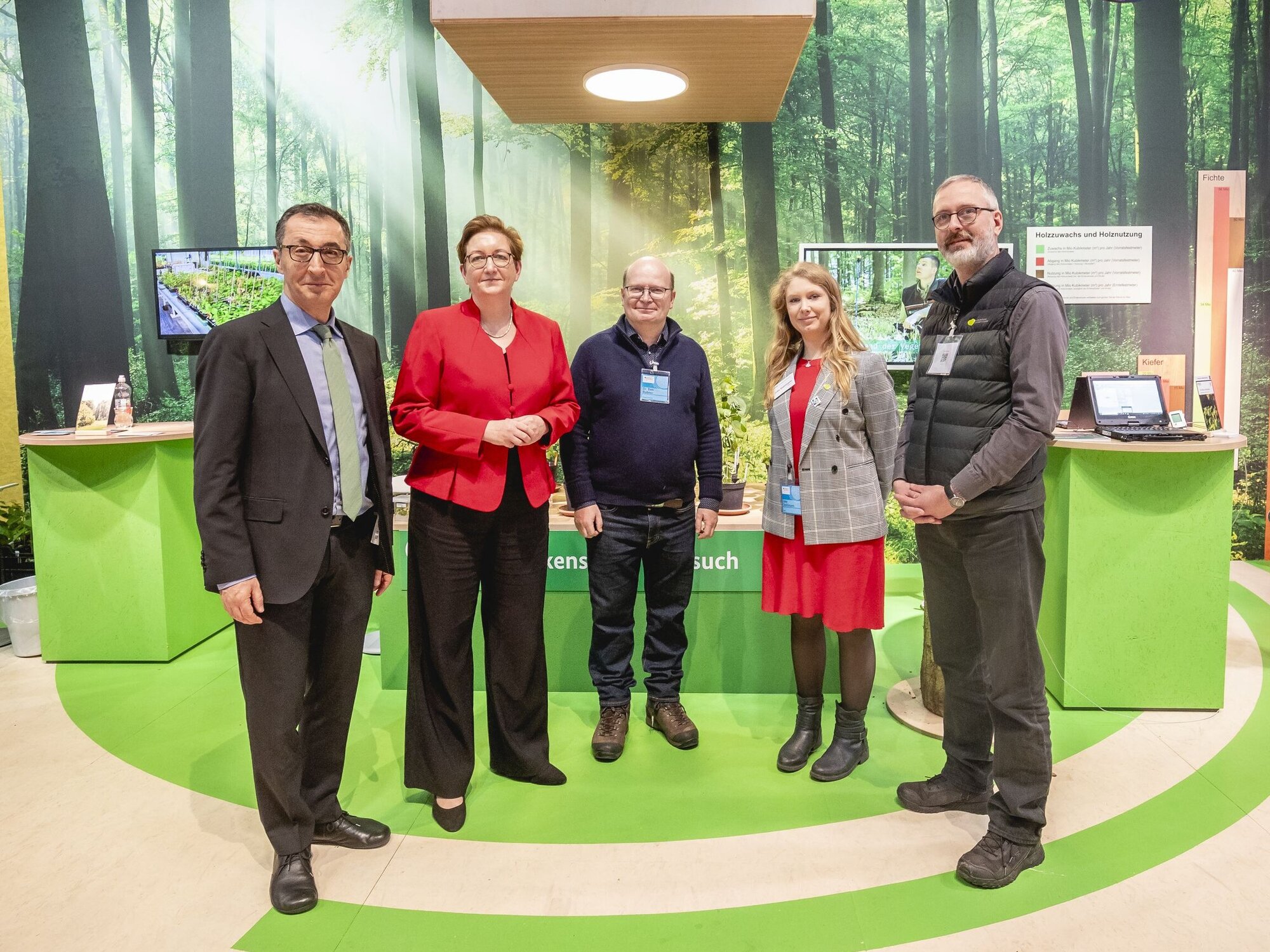 Bundeslandwirtschaftsminister Cem Özdemir und Bundesbauministerin Klara Geywitz am Stand der Bundeswaldinventur. Fünf Personen stehen vor einem Messestand