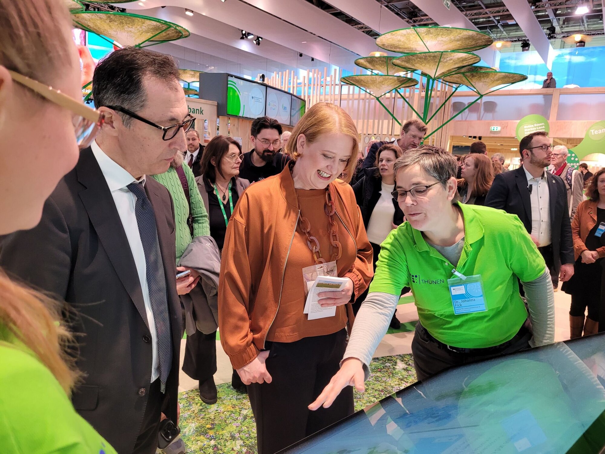 Bundeslandwirtschaftsminister Cem Özdemir und Bundesfamilienministerin Lisa Paus lassen sich den Thünen-Landatlas auf dem großen Touchscreen erklären. Mehrere Personen stehen vor einem großen Touchbildschirm.