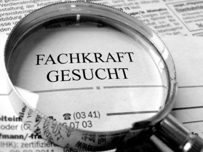 Eine auf einer Zeitung liegenden Lupe hebt die Überschrift „Fachkraft gesucht“ hervor.