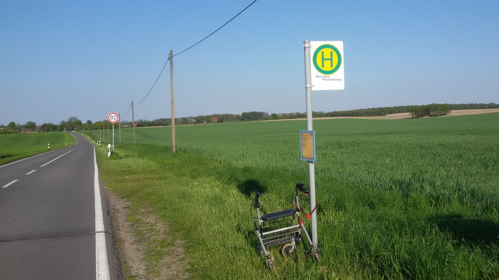 A rollator locked at the bus stop of an empty country road outside a village. 